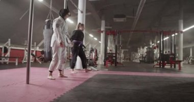 Tracking shot of diverse women doing front rolls on floor during BJJ training in gym