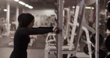 Spor salonundaki işlevsel eğitim sırasında tesettüre halter takan Müslüman kadın sporcunun el kamerasıyla çekilen fotoğrafı.