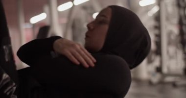 Handheld shot of Muslim sportswoman in hijab crossing arms on chest and doing elevated crunches during fitness training in gym