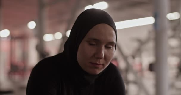 在健身房进行健身训练时 手持照片的年轻穆斯林运动员穿着黑色头巾看着镜头 — 图库视频影像