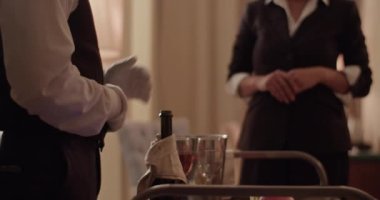 Crop unrecognizable waiter in elegant outfit and white gloves introducing ordered wine and fruits to anonymous guest during room service in hotel