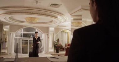 Back view of crop young female receptionist standing at desk and greeting happy African American guest giving passport after arriving in luxury hotel