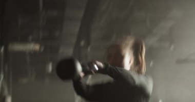 Uzun siyah at kuyruklu güçlü genç bayan sporcu modern spor salonunda çalışırken kettlebell salıncak egzersizi yapıyor.