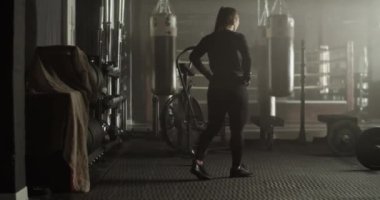 Spor kıyafetleriyle uzun kahverengi saçlı, kaslı genç bayan sporcunun modern ferah spor salonunda yürürken fonksiyonel egzersizler sırasında dinlenmesinin yan görüntüsü.