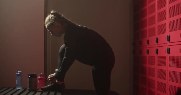 ロッカールームでのワークアウトの準備中にスニーカーの上にアクティブなネクタイレースで長い暗いポニーテールを持つ運動若い女性の側面図 — ストック動画
