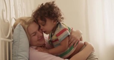 Sarışın, güler yüzlü, neşeli, genç bir anne. Günlük giysiler içinde, gülümseyen ve evde küçük, sevimli etnik oğlunu kucaklayan bir anne.