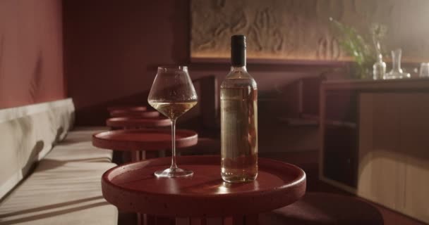 赤の小さな丸いバーテーブルの上に置かれた白ワインボトルのスローモーションハンドヘルドショットぼやけた背景に対するワイングラス — ストック動画