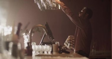 Yan görüntüde, erkek yöneticinin şarap kadehini alıp tezgahın üzerinde sallanırken temizlik kontrolü yaparken ve bar açılmaya hazırlanırken havluyla silerken görülüyor.