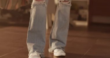 Genç, dövmeli, uzun kahverengi saçlı, yırtık kotlu, spor ayakkabılı, yaratıcı salonda duran ve kameraya özgüvenle bakan kadın üstadın görüntüsünü kaldır.