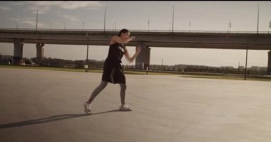 Kentin boş zemininde sabah vakti yapayalnız boks yaparken yumruk antrenmanı yapan genç bayan sporcuların yan görüntüsü.