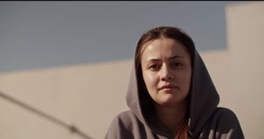 Gri kapüşonlu genç bayan sporcunun düşük açılı el kamerası görüntüsü şehir manzarasının bulanık arka planına bakıyor.