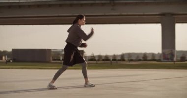 Tam vücut pozu. Kendine güvenen ve kapüşonlu güçlü sporcu kadın. Boş şehirde sabah antrenmanında gölgelerde boks yaparken hızlı bir şekilde hava alıyor.