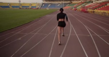 Stadyumdaki sprint müsabakasına hazırlanırken siyah spor giysili bir kadının antrenman sırasında hızla koşarkenki arka plan görüntüsü.
