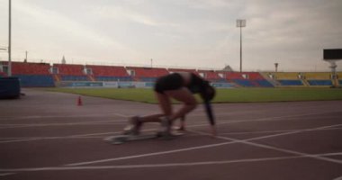 Yan görüş, genç atletik kadın koşucunun blok dışına itildiğini ve güneş doğarken gökyüzüne karşı sürat antrenmanında hızla koştuğunu gösteriyor. 