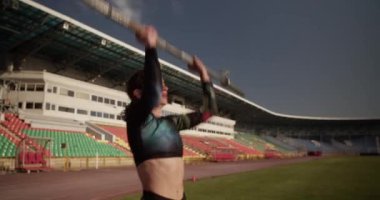 Spor giyimli genç güçlü bir koşucunun sabah stadyumdaki antrenman sırasında ağırlık kaldırışının gerçek zamanlı el çekimi.