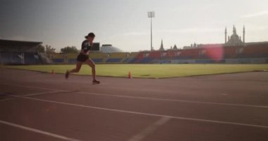 Açık hava antrenmanı sırasında hızlı koşan aktif giyimli genç bayan koşucunun sprint yarışmalarına hazırlanışının yan görüntüsü.