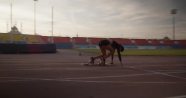 Yan görüş, genç atletik kadın koşucunun blok dışına itildiğini ve güneş doğarken gökyüzüne karşı sürat antrenmanında hızla koştuğunu gösteriyor. 