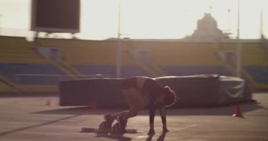 Yan görüş, genç atletik kadın koşucunun blok dışına itildiğini ve güneş doğarken gökyüzüne karşı sürat antrenmanında hızla koştuğunu gösteriyor. 