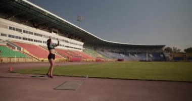 Aktif giyimli genç ve güçlü bir sporcunun stadyumdaki atlayışlarla ağırlık kaldırma hareketi yaparken el kamerası görüntüsü.