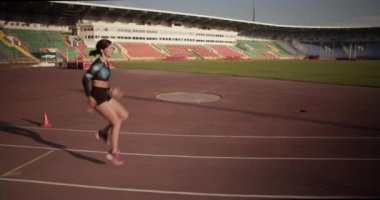 Spor kıyafetleriyle koşan ve stadyumdaki antrenman sırasında diz kaldırma egzersizi yapan bayan koşucunun yan görüntüsü.