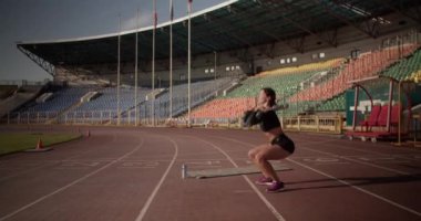 Stadyumdaki antreman sırasında ağırlık kaldırarak koşu pistinde ayakta duran güçlü spor kadınının el kamerası görüntüsü.