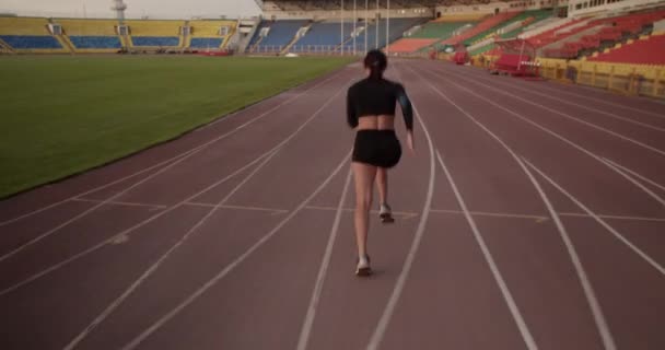 バックビュー陸上競技場でスプリント競技の準備中にトレーニング中にトラック上で速く走る黒のスポーツウェアのスポーツ女性のショットを追跡 — ストック動画