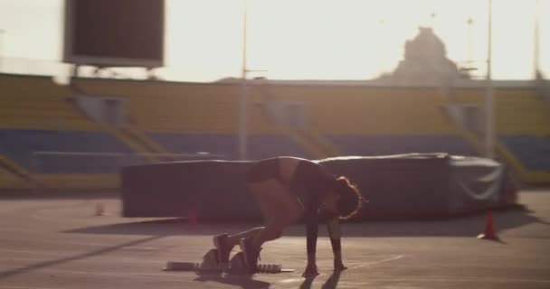 日の出の空に対してスプリントトレーニング中にブロックからプッシュし トラック上で高速実行アクティブウェアで若いアスレチック女性ランナーのサイドビュー追跡ショット — ストック動画