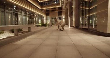 Modern milenyum erkeğinin kulaklıklarıyla gece parlayan şehrin bahçesinde çağdaş break dans yaparken görüntüsünü yakınlaştır.