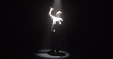 Kulaklıklı modern beyaz adam sahne ışıkları altında serbest dans ederken müzik dinlerken kollarını kaldırıyor.