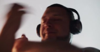 Düşük açılı beyaz erkek beyaz dansçı kulaklıkla müzik dinlerken çağdaş koreografiyi beyaz arka planda kapalı gözlerle dans ediyor.