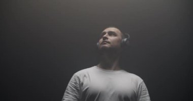 Kulaklıklı modern hip hop dansçısının düşük açılı görüntüsü siyah arka planda ışık altında hareket ederken kollarını hareket ettiriyor.