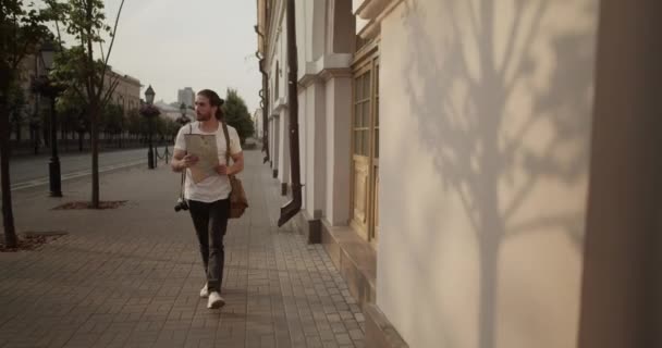 若いひげ付き男性観光客のリアルタイムトラッキングショット写真カメラと肩にバッグ 街を旅しながら地図をチェック — ストック動画