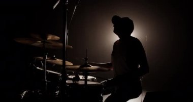 Kimliği belirsiz erkek davulcunun silueti arka plandaki ses kontrolü sırasında karanlık sahnede çalarken profesyonel bateri setinde ritim çalıyor.