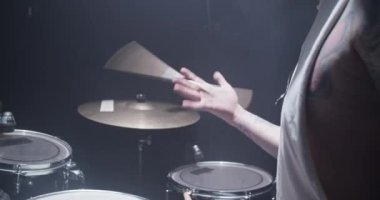 Tanımlanamayan erkek davulcunun yan görüntüsü. Üzerinde dövmeler var. Prova sırasında ellerinde tahta bagetler var.