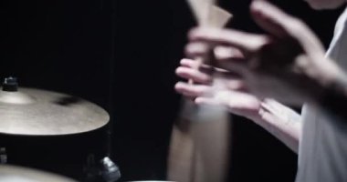 Karanlık bir kulüpte rock konserine hazırlanırken ahşap baget çeviren tanınmayan dövmeli erkek davulcunun yan görüntüsü