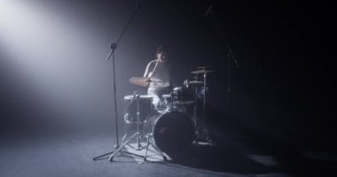 Sıradan giyinmiş, şapkalı, davul çalan ve sahnede kapalı gözlerle müzik dinlemekten hoşlanan genç erkek davulcu.