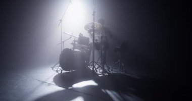 Havalı, genç bir erkek rockçı. Günlük kıyafetleri ve şapkaları var. Sahne ışıkları altında iskemlede otururken davul çalıyorlar.