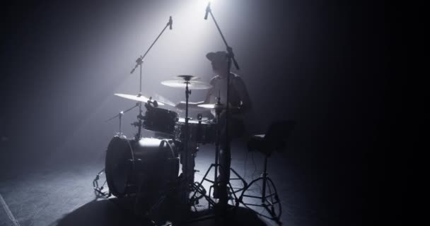 Male drummer tapping on bass drum pedal and playing on professional drum set while performing on stage with computer and microphones