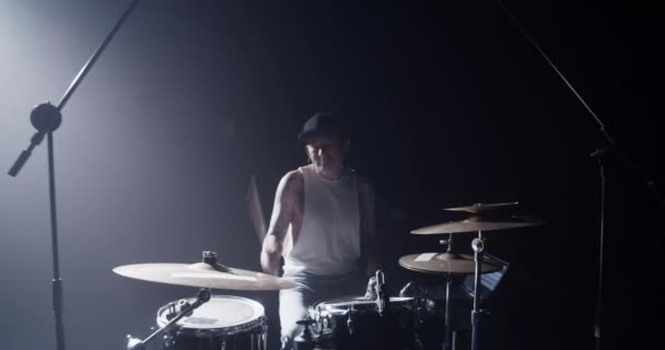 Full body of talented young male drummer in casual clothes and cap spinning drumstick on hand and playing drums with closed eyes during rehearsal on stage