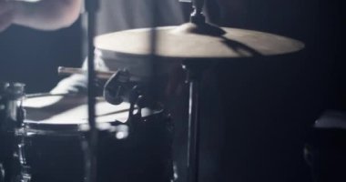 Sıradan giysiler içinde, sopayla davul çalan ve sahnede rock konseri verirken ritim tutan isimsiz bir erkek müzisyen.