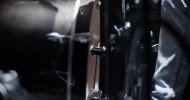 Prova sırasında perküsyon enstrümanlarında ritm çalarken, günlük giysiler içinde, davul pedalı iten yüzü olmayan erkek müzisyenin yan görüntüsü