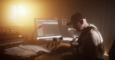 Kayıt stüdyosunda melodi yaratırken şapkalı, masada bas gitar çalan ilham verici erkek sanatçının el kamerası görüntüsü. 