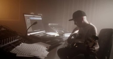 Kayıt stüdyosunda müzik notaları izlerken bas gitar çalan erkek ses mühendisinin yan görüntüsü
