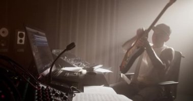 Kablolu yayın yapan ve elektro gitar çalmaya başlayan erkek gitarist profesyonel müzik stüdyosunda profesyonel ses ekipmanlarıyla şarkı yaratıyor.
