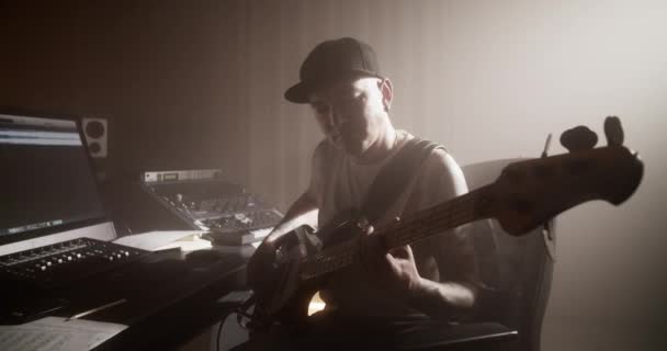 レコーディングスタジオのベースギターとサウンドミキサーを使用したカジュアルな服とキャップ作曲のサウンドエンジニア — ストック動画