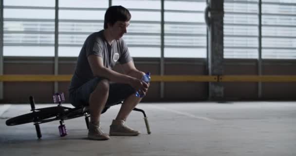 Zdjęcie Młodego Wyczerpanego Jeźdźca Bmx Siedzącego Rowerze Butelką Wody Ciężko — Wideo stockowe
