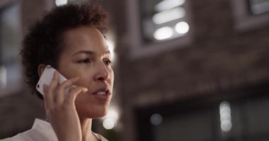 Afrika kökenli Amerikalı bir kadın yöneticinin, sokakta telefon görüşmesi yaparken, akşam vakti dışarıda duran önemli iş konularını tartışırken gerçek zamanlı bir fotoğrafı.