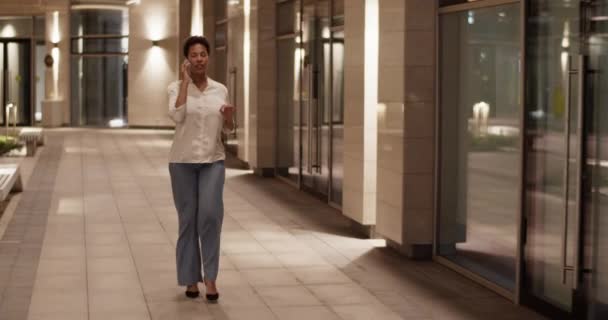全面追踪成功的非裔美国女商人深夜工作时在办公大楼附近边走来走去 谈论如何用智能手机解决商务问题的照片 — 图库视频影像