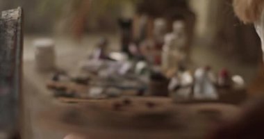Sanat atölyesinde yağlı boya tüpleri, çözücü şişeler ve fırçalar ile masanın yanında sanat eserleri oluştururken palet tutan isimsiz bir sanatçının gerçek zamanına odaklan.