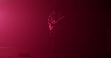 Erkek gitaristin elektro gitar çalıp rock 'n roll yaptığı ve boş zamanlarında pembe neon ışıklarıyla aydınlatılan karanlık stüdyoda prova yaptığı tüm vücut çekimi.